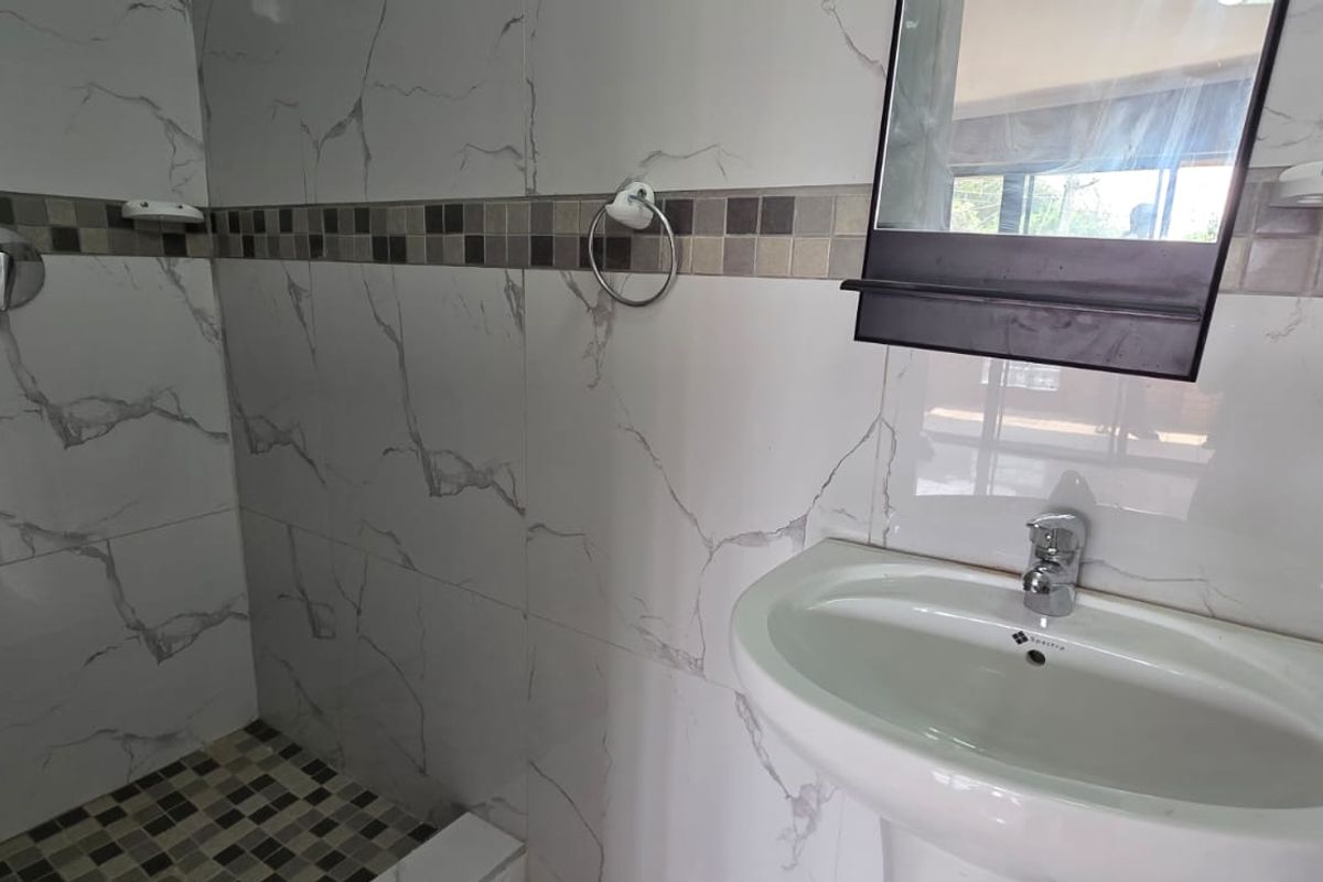 A clean, modern bathroom featuring a pedestal basin, wall-mounted mirror, and a tiled shower enclosure with decorative mosaic accents.