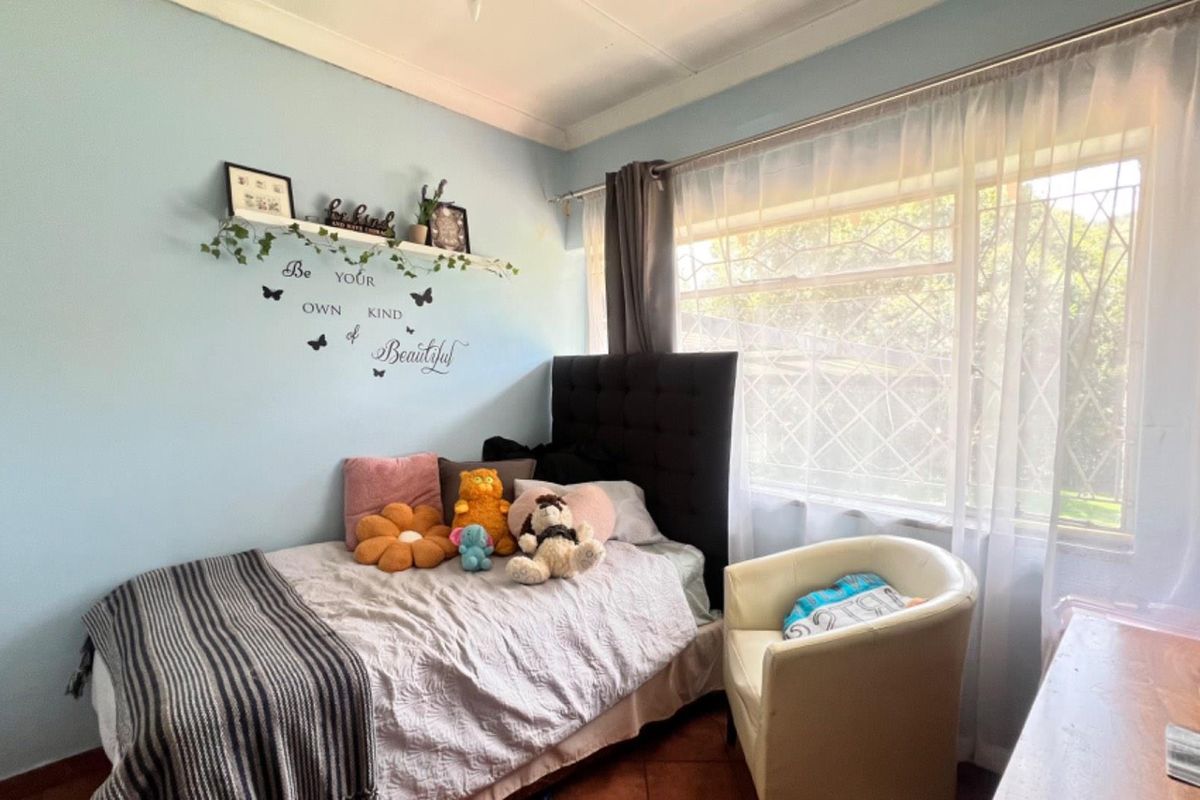A cozy bedroom featuring a large window with security bars, neutral wall tones, and tiled flooring.