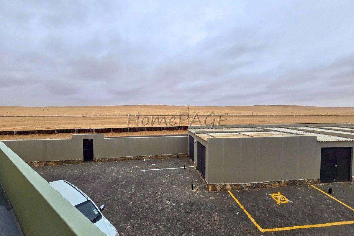 An elevated view of a paved parking area with garage units, enclosed by a perimeter wall, overlooking an expansive desert landscape.