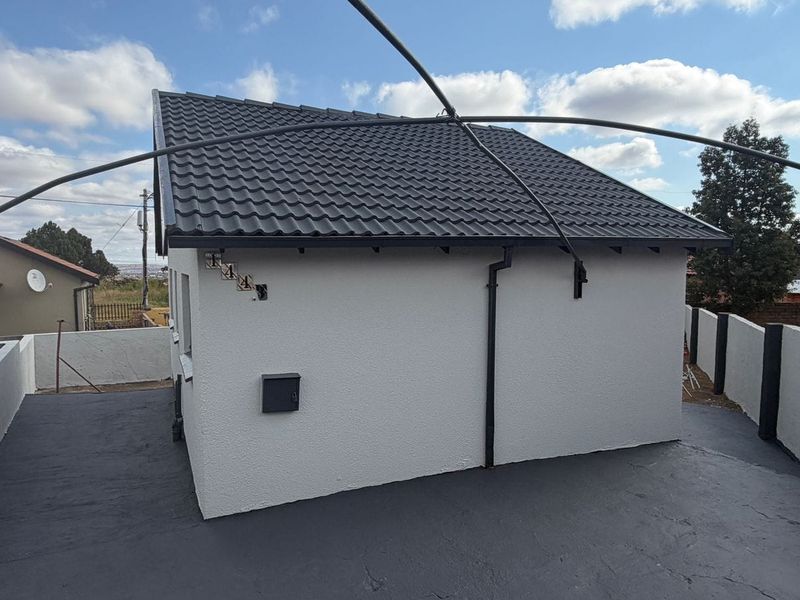 A view of the rear exterior of the house featuring a tiled roof, painted walls, and a paved outdoor area.