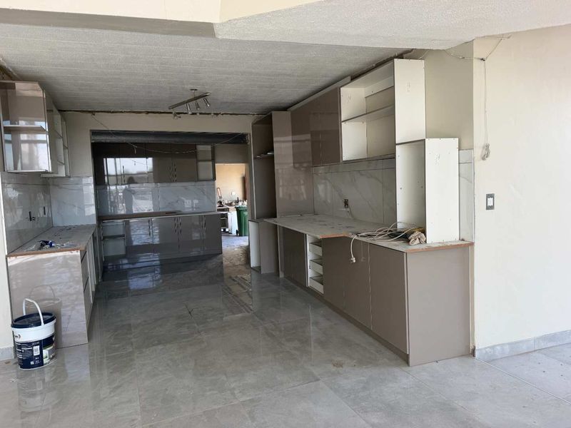 An unfinished kitchen space featuring modern high-gloss cabinetry, marble-look wall tiles, and large format floor tiles, currently undergoing renovation.