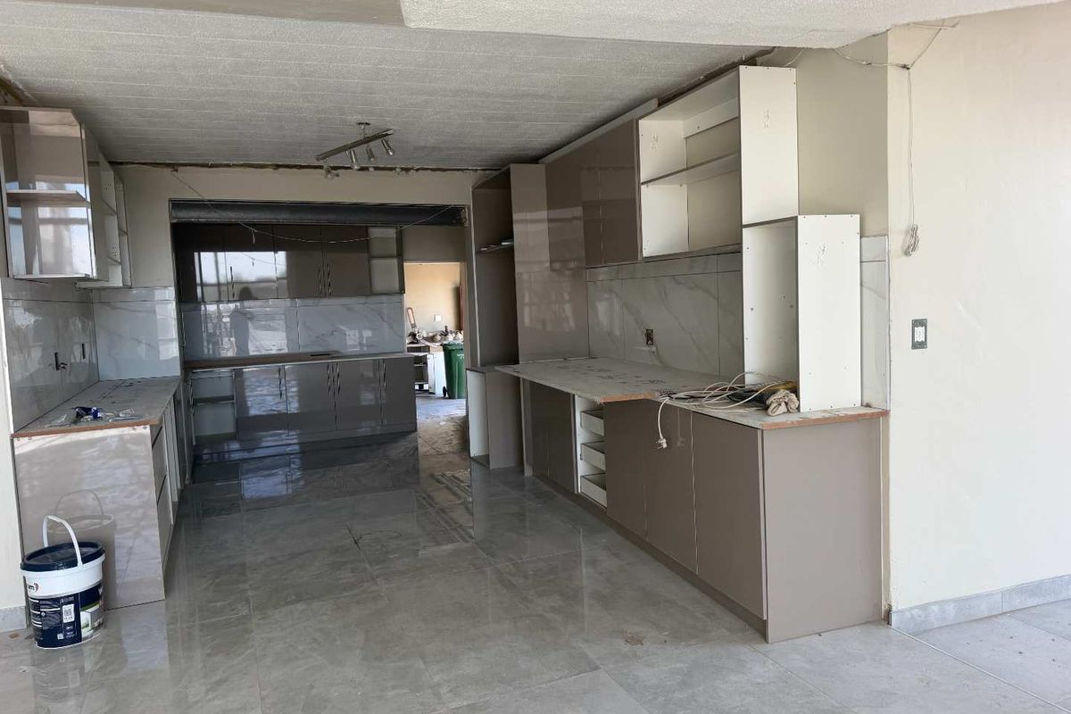 An unfinished kitchen space featuring modern high-gloss cabinetry, marble-look wall tiles, and large format floor tiles, currently undergoing renovation.