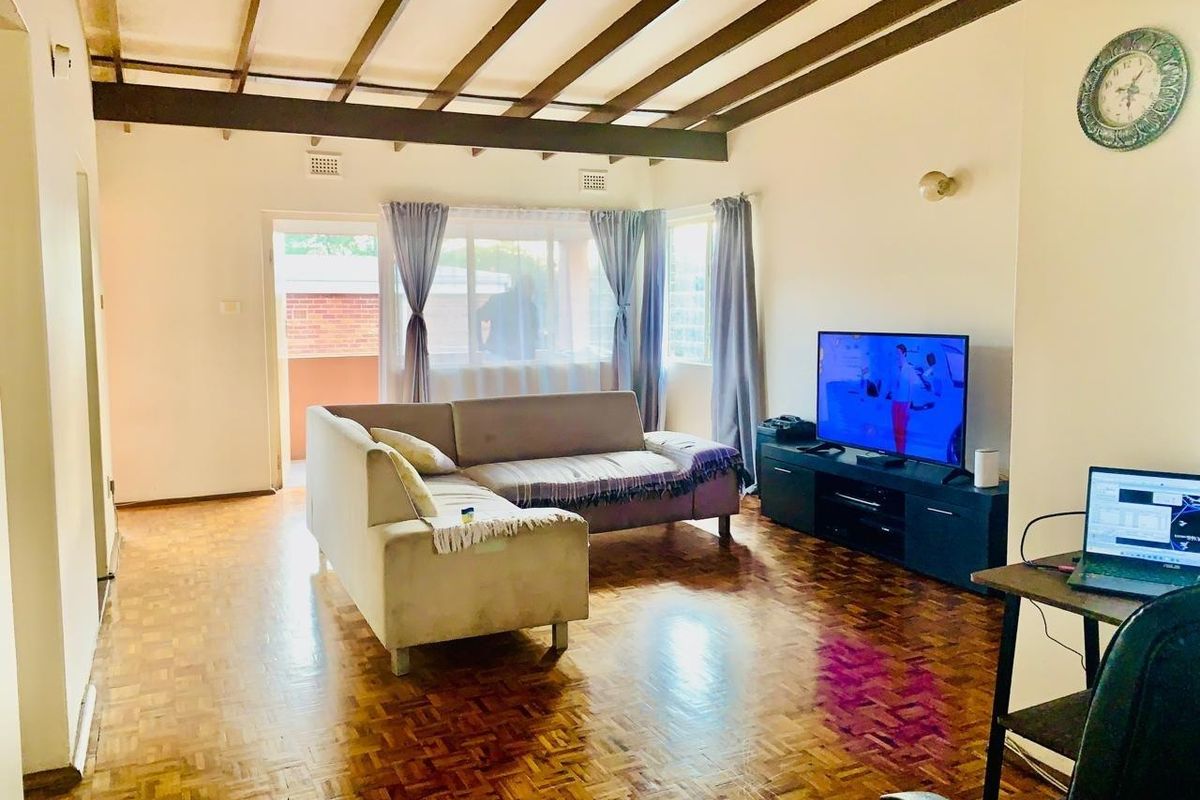 Spacious living room featuring classic parquet flooring, exposed timber ceiling beams, and direct access to an outdoor balcony area.