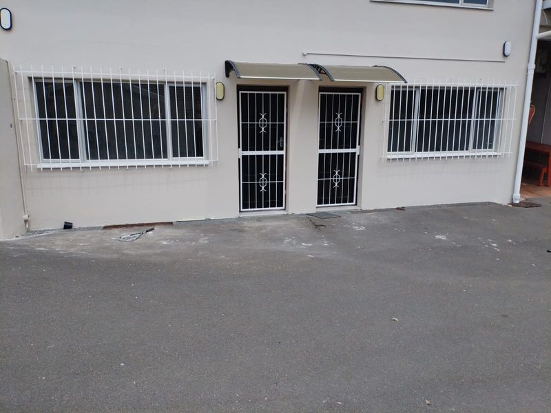 Front exterior view of the cottage featuring security bars on windows and doors, with a paved driveway area.