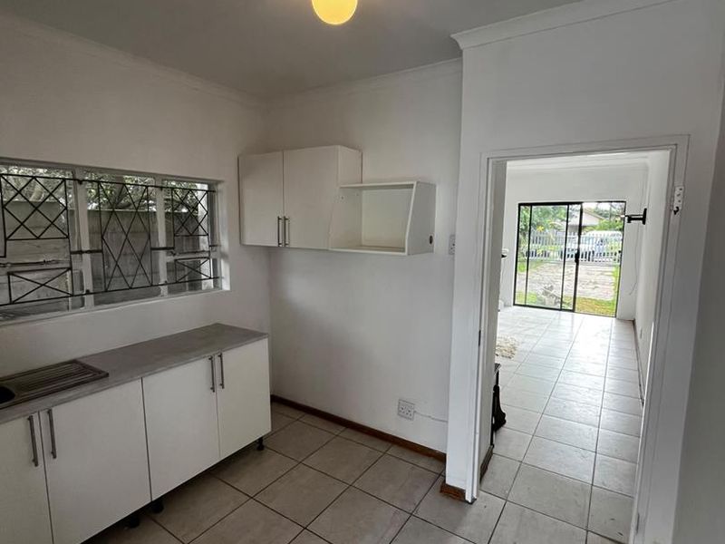 A functional scullery or utility area featuring built-in white cabinetry, a stainless steel sink, and ceramic tiled flooring, leading through to the main living space.