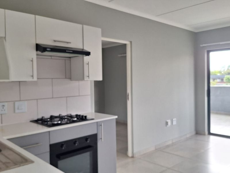 Modern open-plan kitchen and living area featuring neutral cabinetry, built-in appliances, tiled flooring, and direct access to a balcony through sliding glass doors.