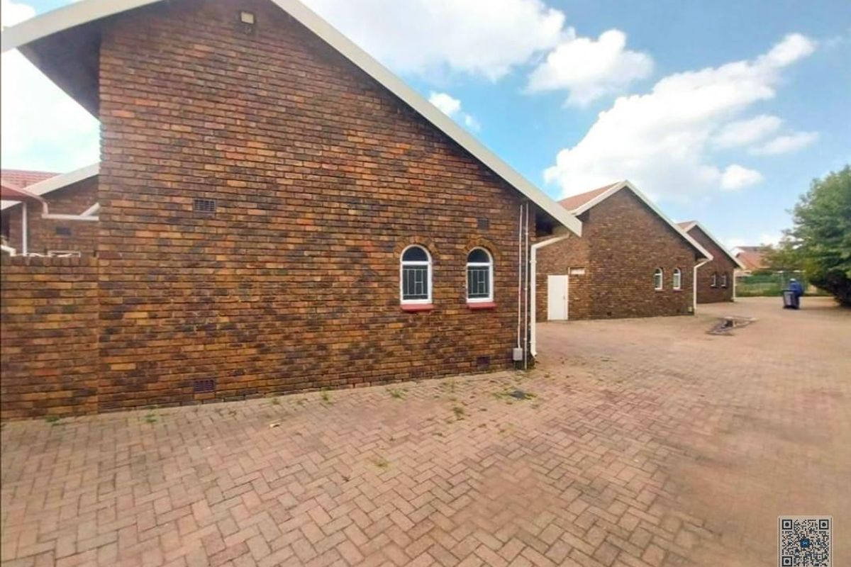 Exterior view of a face-brick residential building featuring paved driveway access and arched window detailing.