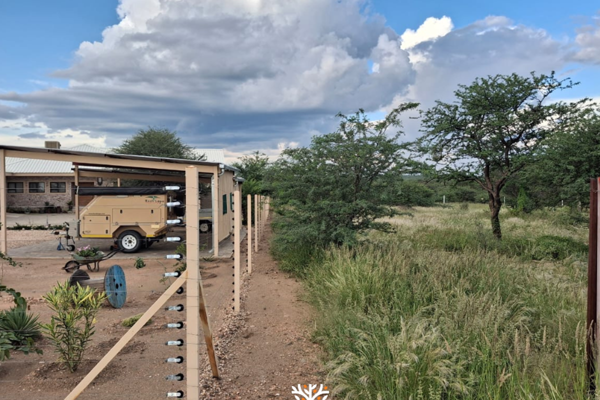 A view of the property grounds featuring an electric fence boundary, gravel driveway area, and natural bushveld vegetation.