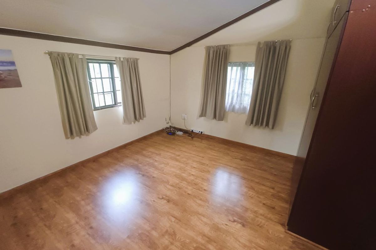 A bedroom featuring wood-look laminate flooring, built-in cabinetry, and dual windows with curtain fixtures.