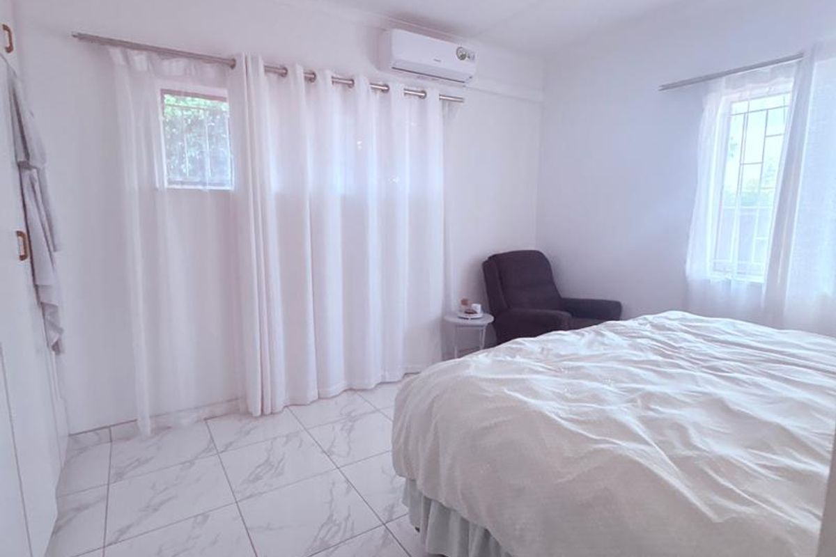 A bright bedroom featuring marble-look floor tiles, built-in cupboards, and a wall-mounted air conditioning unit.