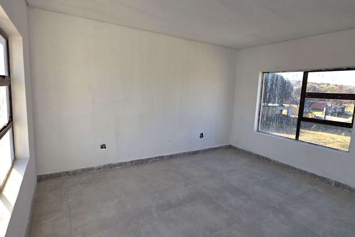 An empty, unfinished bedroom featuring tiled flooring and aluminium-framed windows, awaiting final finishes and interior design.
