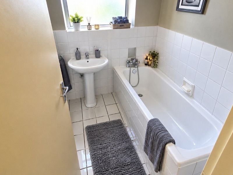 A functional bathroom featuring a white pedestal washbasin, a standard bathtub with a mixer tap, and clean white wall tiling.