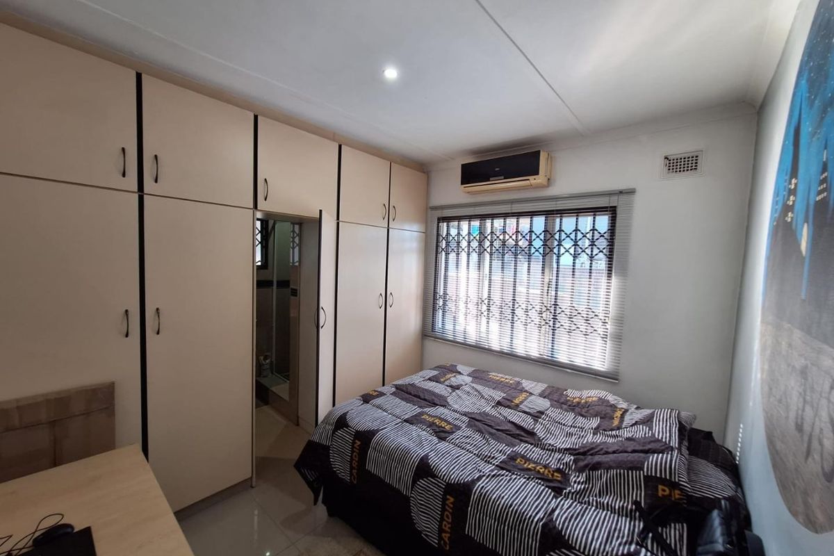 A functional bedroom featuring extensive built-in cabinetry, tiled flooring, an air conditioning unit, and a window fitted with security bars and blinds.