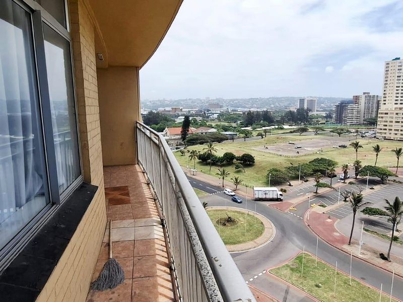 A balcony with tiled flooring and metal railings, offering an elevated view of the surrounding urban landscape and parking area.