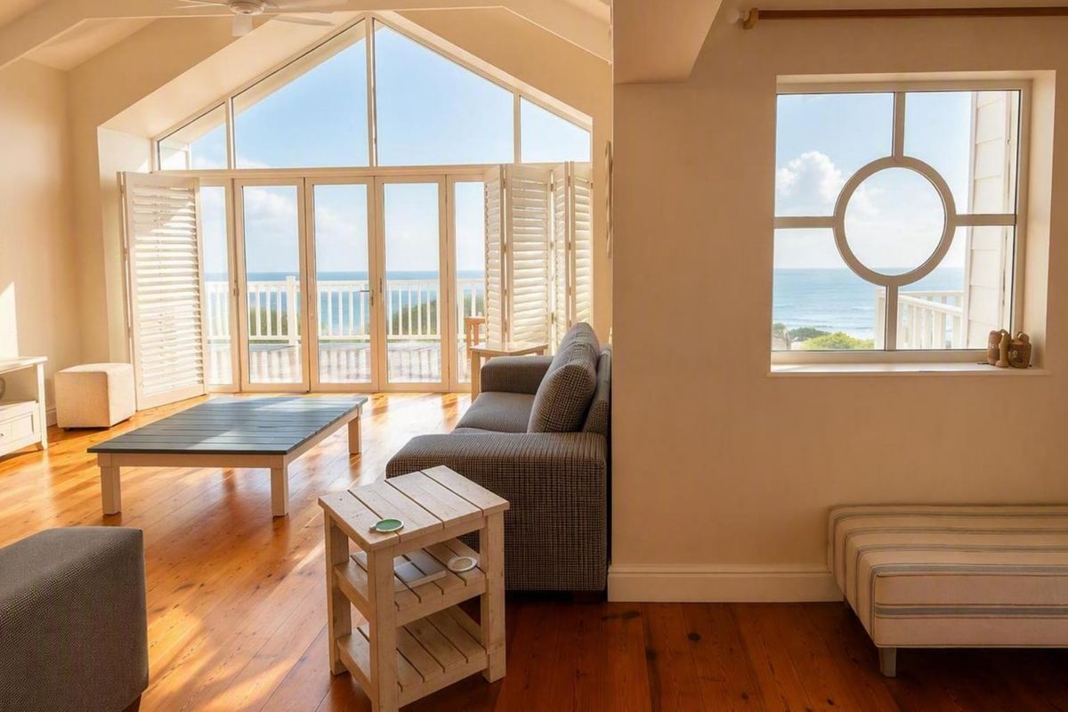 Spacious living room featuring vaulted ceilings, timber flooring, and expansive bi-fold doors opening to a scenic ocean view.