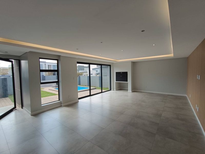 Spacious, modern open-plan living area featuring large format floor tiles, recessed ceiling lighting, a built-in fireplace, and sliding doors leading to the pool area.