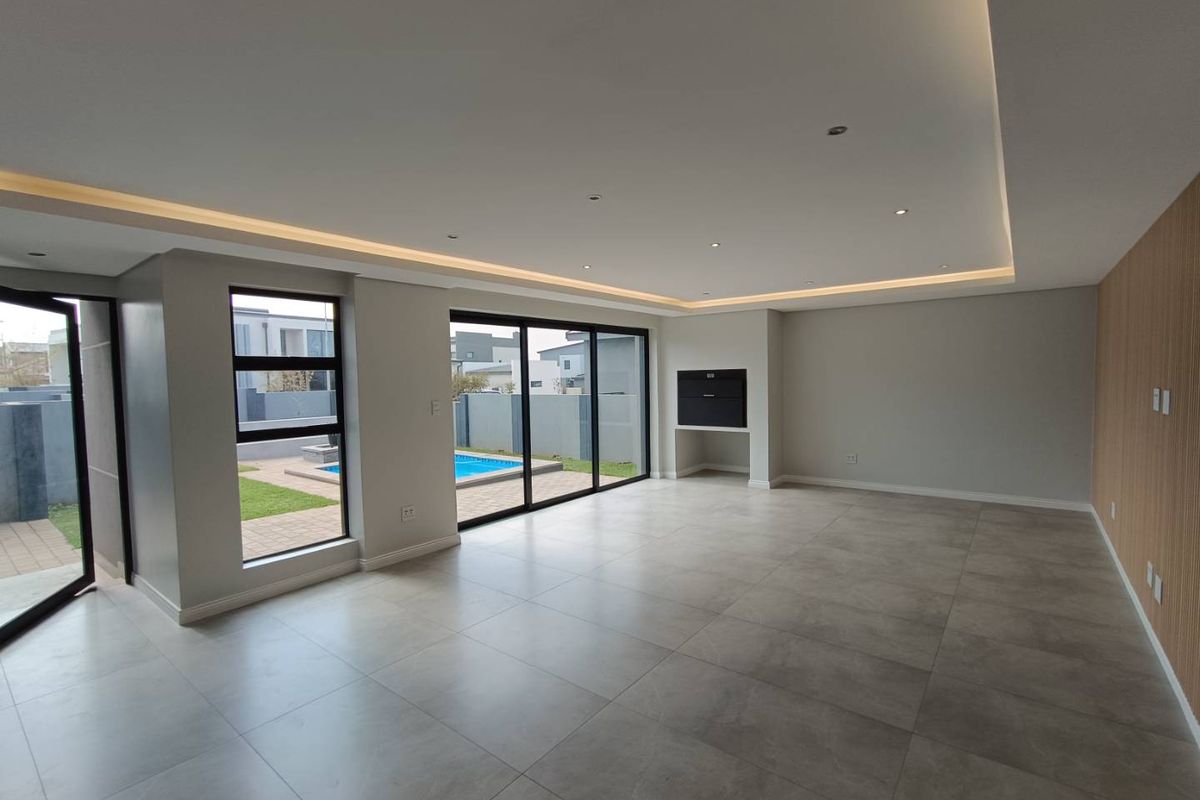 Spacious, modern open-plan living area featuring large format floor tiles, recessed ceiling lighting, a built-in fireplace, and sliding doors leading to the pool area.