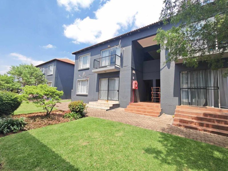 Rear view of the apartment complex featuring a landscaped garden, paved walkways, and private balconies with security gates.