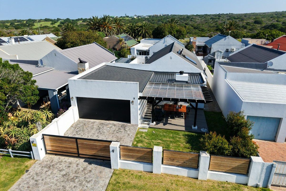 Aerial view of a modern residential property featuring a paved driveway, secure boundary wall, garage, and a covered outdoor patio area.
