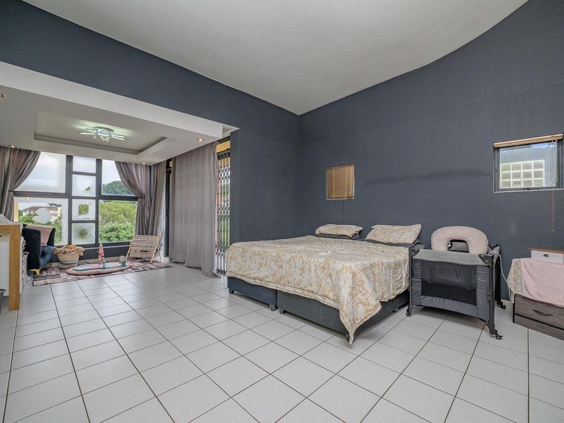 Spacious bedroom featuring tiled flooring, a recessed ceiling detail, and large aluminium windows providing ample natural light.