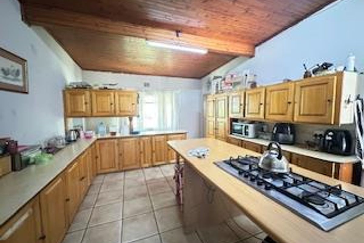 Spacious kitchen featuring extensive wooden cabinetry, a central island with a built-in gas hob, and tiled flooring under a timber-clad ceiling.