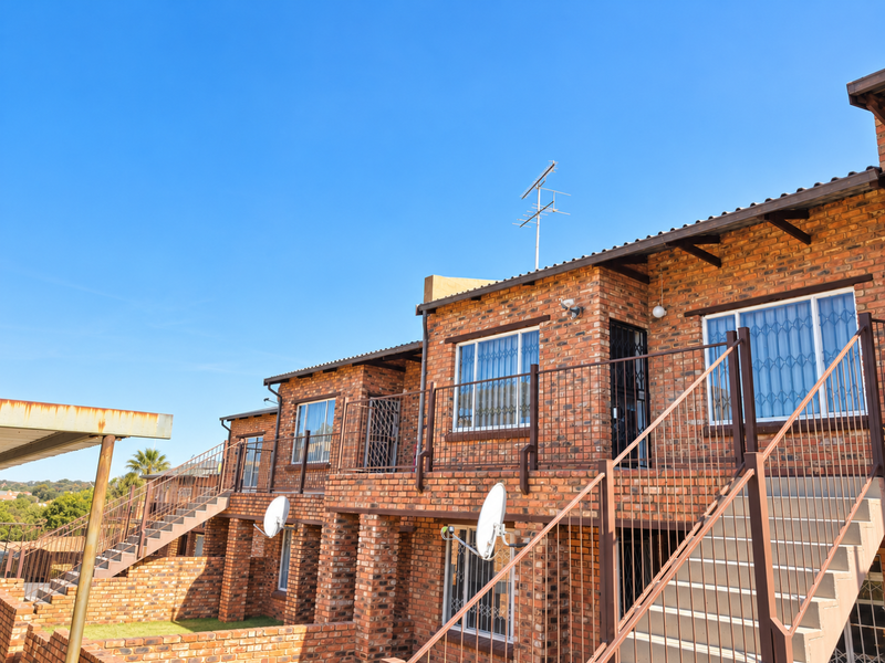 Exterior view of a multi-level apartment complex featuring face brick construction, external metal staircases, and security fixtures.