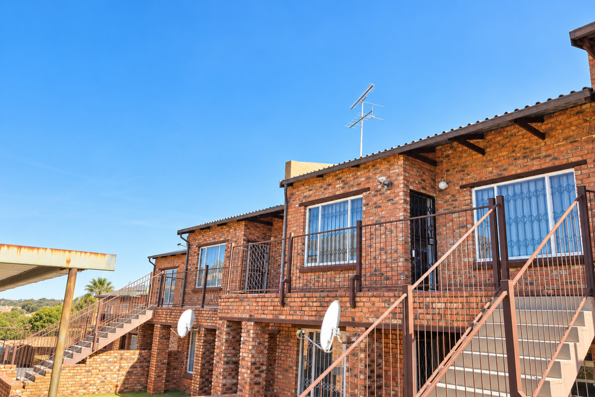 Exterior view of a multi-level apartment complex featuring face brick construction, external metal staircases, and security fixtures.