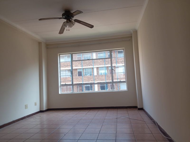 A spacious, empty bedroom featuring tiled flooring, a ceiling fan, and a large window providing natural light and an urban view.