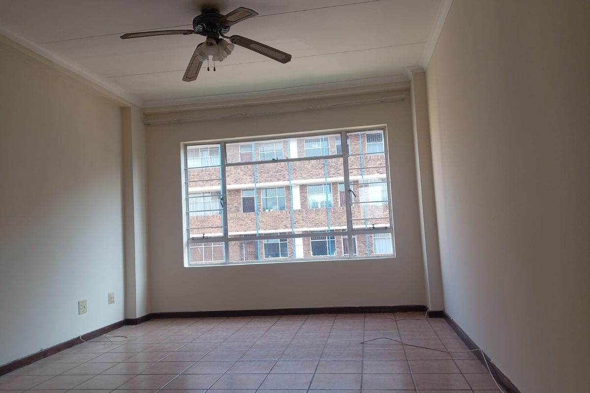 A spacious, empty bedroom featuring tiled flooring, a ceiling fan, and a large window providing natural light and an urban view.