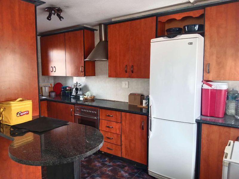 A functional kitchen featuring wood-finish cabinetry, granite countertops, a built-in oven with extractor fan, and tiled flooring.