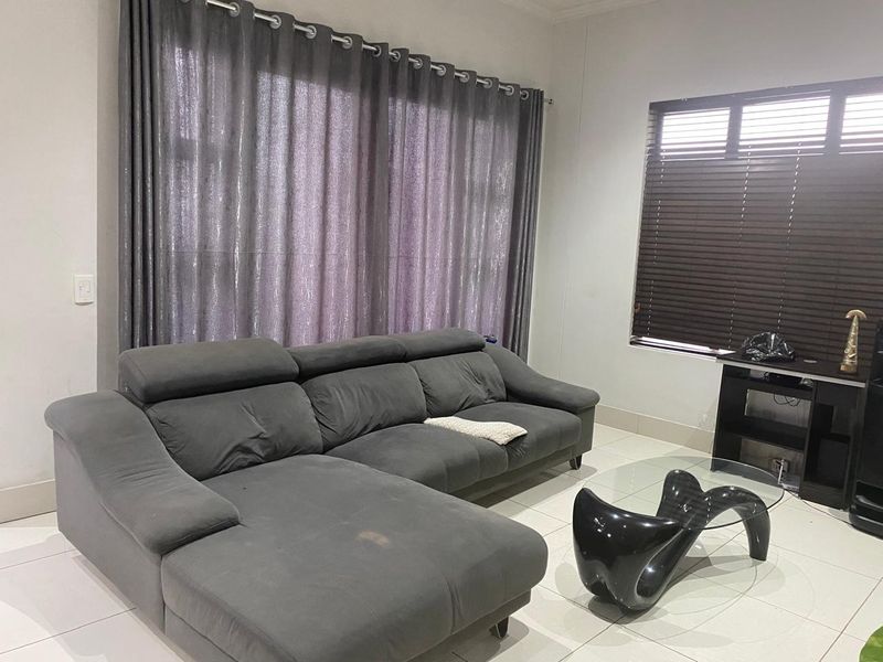 A living room featuring tiled flooring, large window treatments with curtains, and venetian blinds, providing a neutral base for interior design.