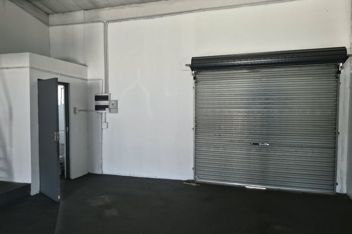 Industrial garage space featuring a large roller shutter door, exposed electrical conduit, and concrete flooring, suitable for storage or workshop use.