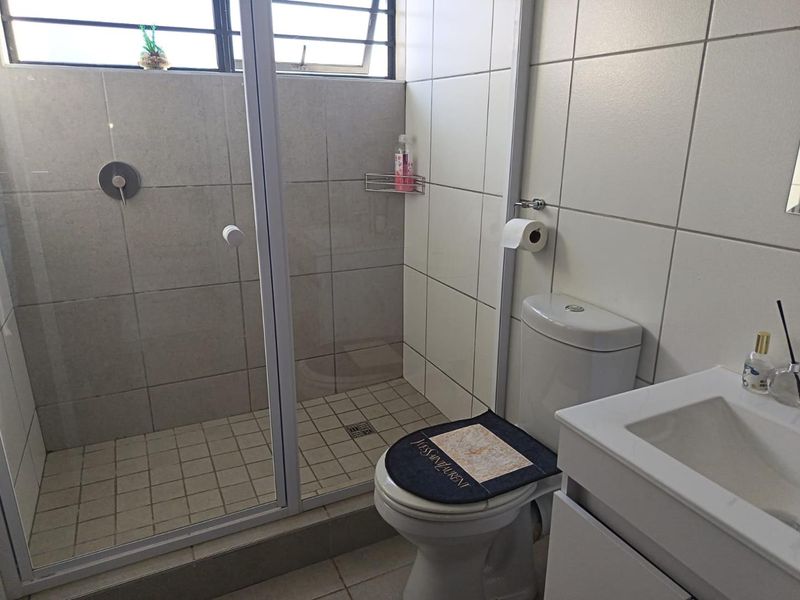 A clean, functional bathroom featuring a glass-enclosed shower, modern toilet, and a vanity basin with tiled finishes throughout.