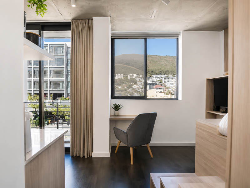 Modern open-plan living area featuring exposed concrete ceilings, dark timber flooring, and a built-in desk with scenic mountain and urban views.