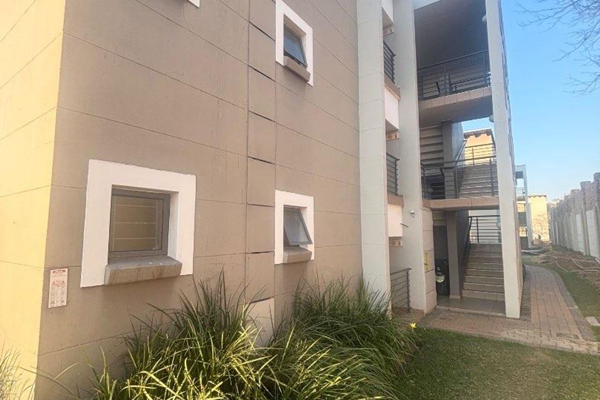 Exterior view of an apartment building featuring a multi-level staircase, balconies, and a landscaped garden area with a paved walkway.