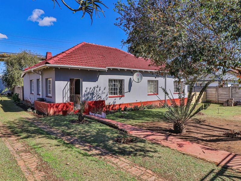 Rear view of a single-story house featuring a tiled roof, grey painted exterior walls with red brick accents, and a spacious garden area.