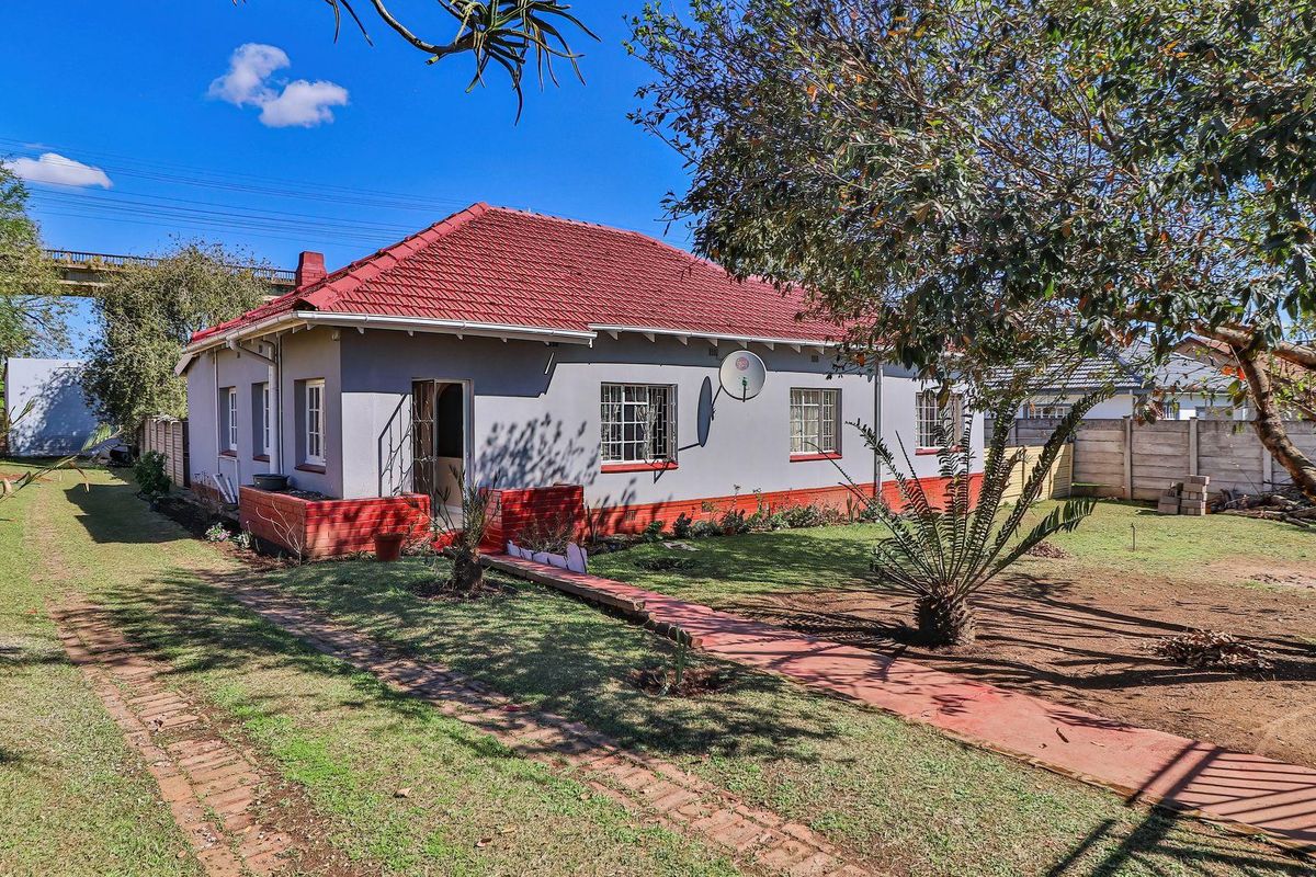 Rear view of a single-story house featuring a tiled roof, grey painted exterior walls with red brick accents, and a spacious garden area.