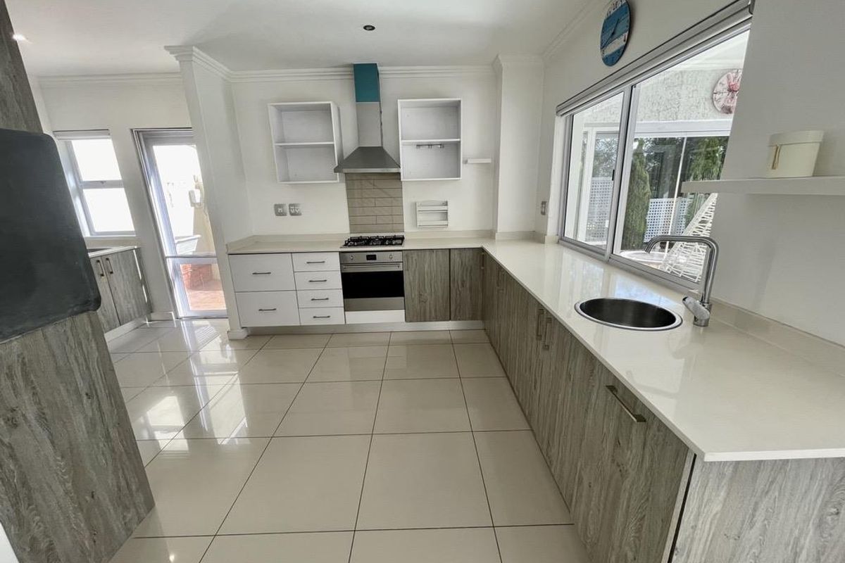 Modern kitchen featuring light wood-grain cabinetry, stone countertops, stainless steel appliances, and large windows providing ample natural light and garden views.