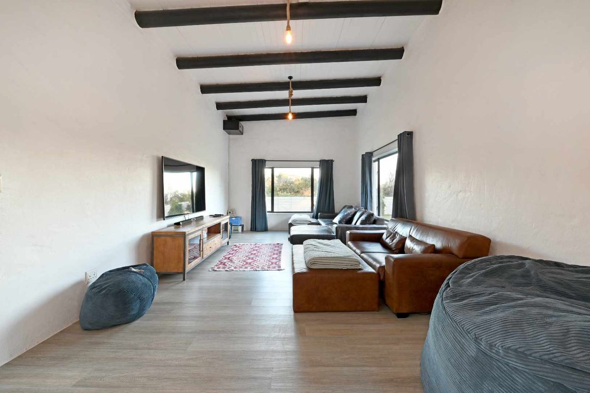 Spacious living room featuring exposed timber ceiling beams, light wood-look flooring, and large windows providing natural light.
