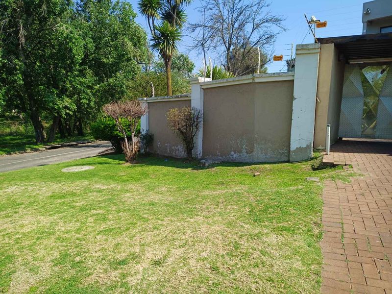 Front exterior view showing a paved driveway, lawn area, and a perimeter wall with security features and visible plaster damage.