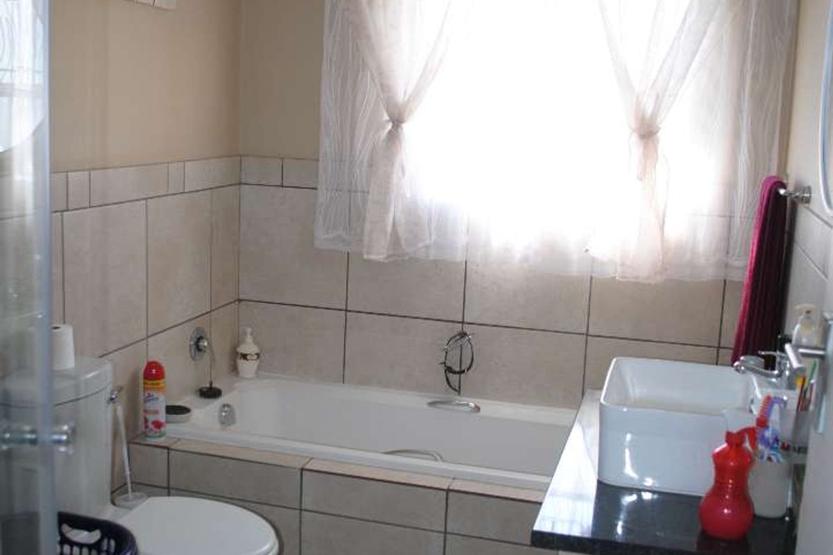 A functional bathroom featuring a built-in bathtub, a modern vessel sink vanity with a stone countertop, and neutral wall tiling.