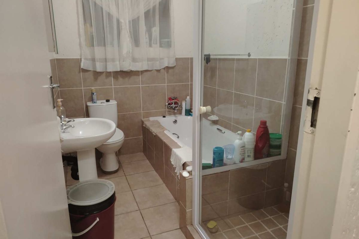 A functional bathroom featuring a pedestal basin, a toilet, and a combined shower and bathtub enclosure with tiled walls and flooring.