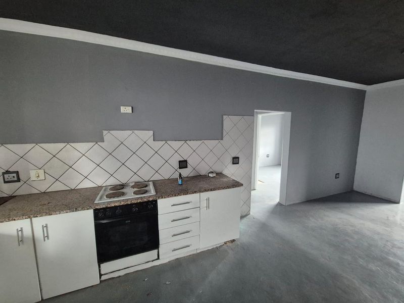 An empty kitchen area featuring white cabinetry, granite countertops, and a built-in oven, currently requiring finishing touches to the backsplash and flooring.