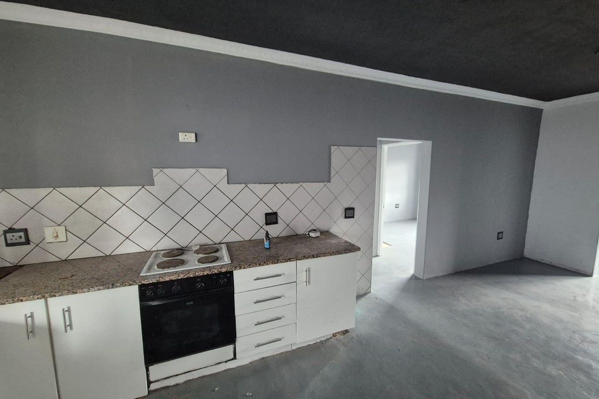 An empty kitchen area featuring white cabinetry, granite countertops, and a built-in oven, currently requiring finishing touches to the backsplash and flooring.