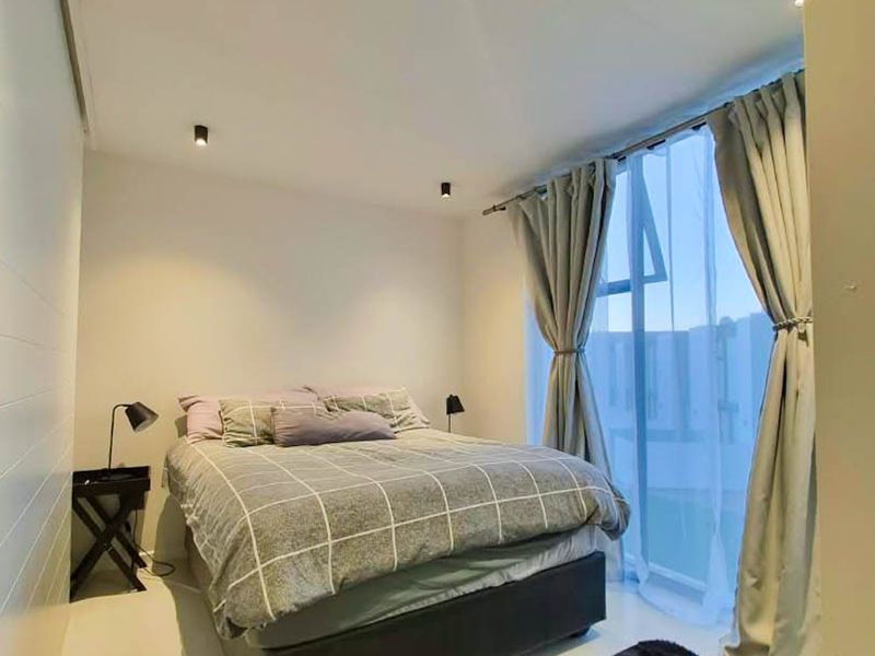 A modern bedroom featuring recessed downlighting and a large floor-to-ceiling window with sliding door access, providing ample natural light.