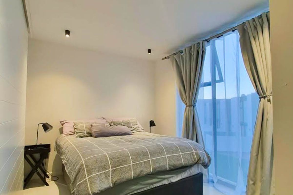 A modern bedroom featuring recessed downlighting and a large floor-to-ceiling window with sliding door access, providing ample natural light.