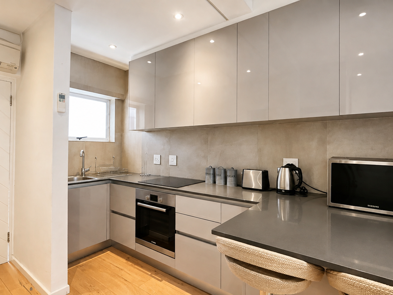 Modern kitchen featuring sleek grey cabinetry, stone countertops, integrated electric hob and oven, and a tiled backsplash with recessed lighting.
