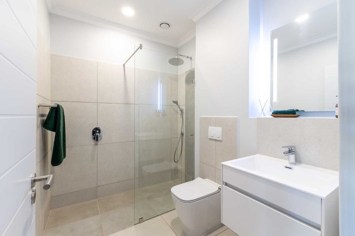 Modern bathroom featuring a walk-in shower with glass screen, wall-mounted toilet, and a sleek vanity unit with basin.
