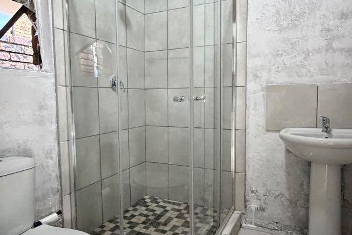 A bathroom featuring a shower enclosure, pedestal basin, and toilet under a traditional thatched roof, requiring significant wall repairs and cosmetic updates.