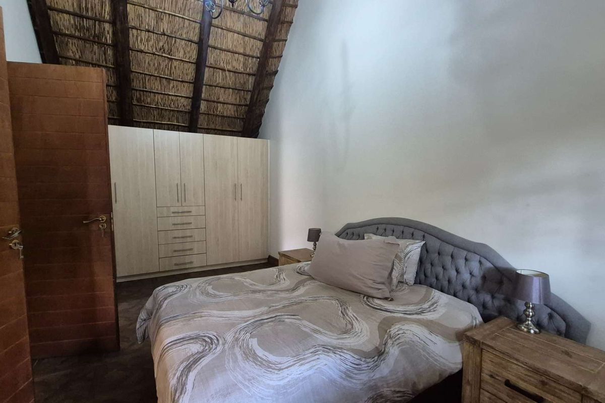 Spacious bedroom featuring a high-pitched thatched roof with exposed timber beams and ample built-in cupboard storage.